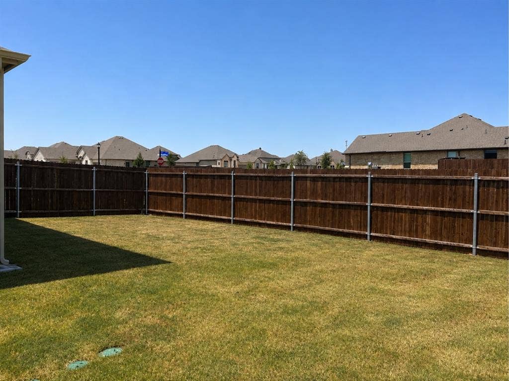 6002 14th Street, Midlothian, TX 76065 Spacious backyard featuring a level lawn with mature wood-finish fencing and metal posts, bordered by residential properties