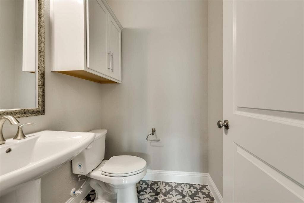 Pedestal sink with a brushed nickel faucet, framed mirror, wall-mounted cabinetry, and decorative floor tiling