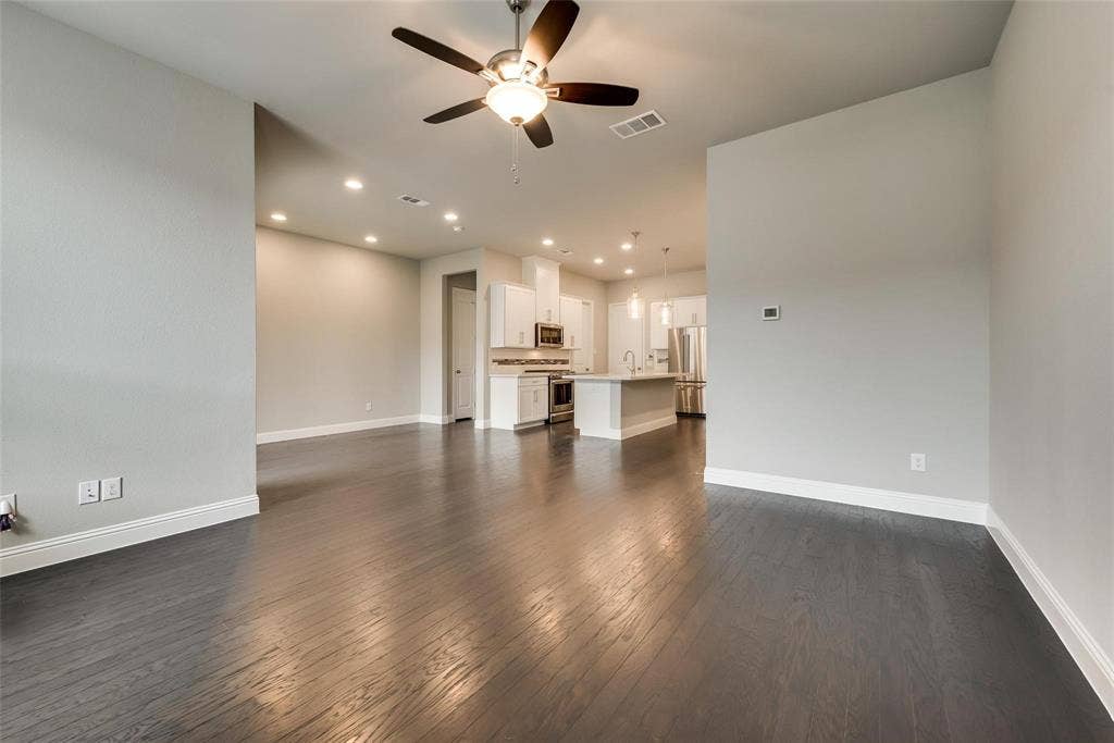 Expansive living area with dark wood-finish flooring, a ceiling fan with integrated lighting, and recessed ceiling lights