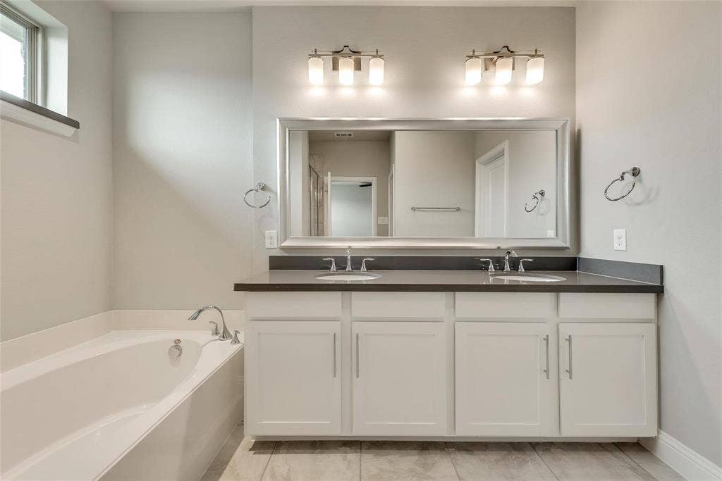 Spacious bathroom featuring a built-in soaking tub, dual vanity with undermount sinks, and a large framed mirror