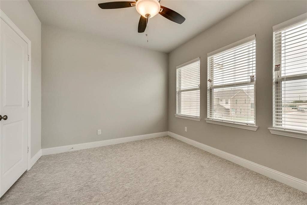Recessed panel door with dark hardware, three windows with blinds, ceiling fan with integrated lighting, and carpeted flooring
