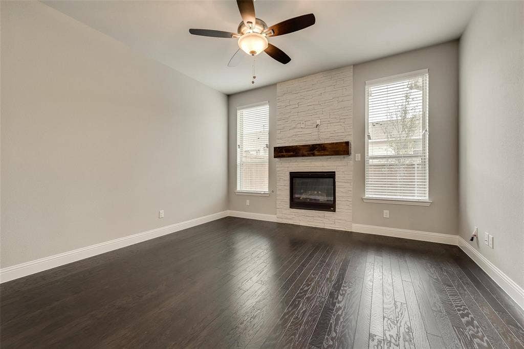 Wood-finish flooring, white brick fireplace surround, dark wood mantel, built-in fireplace, and ceiling fan with integrated lighting