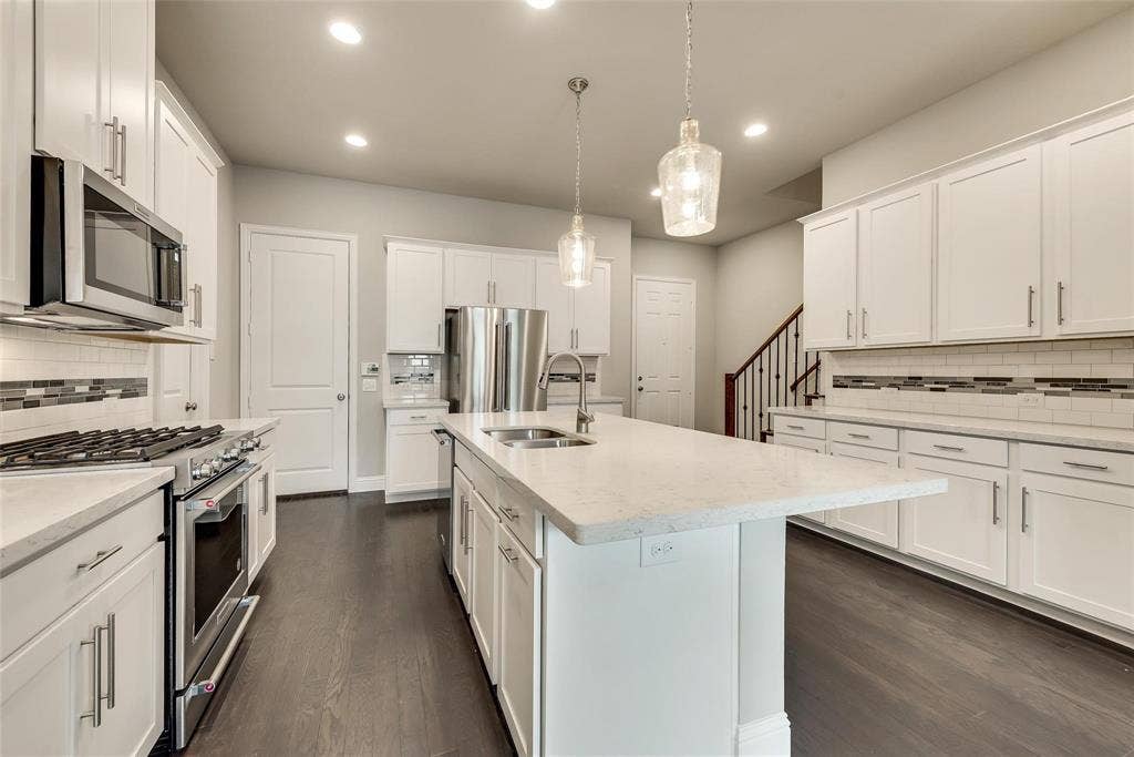 Kitchen featuring white cabinetry, stainless steel appliances, a center island with sink, pendant lighting, and wood-finish flooring