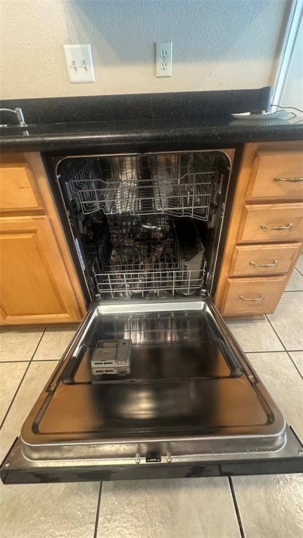 DW has Stainless steel interior, complemented by a black countertop, natural wood-finish cabinetry, and tiled flooring