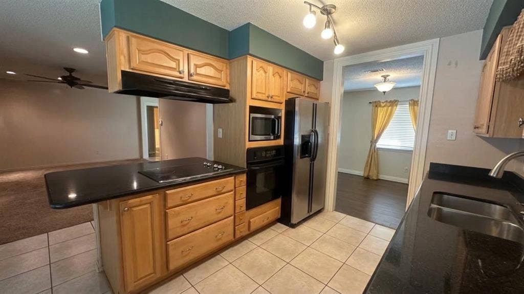 Kitchen featuring wood cabinetry, black solid  countertops, tile flooring, and updated black appliances - smooth top cooktop, MW, oven and DW, refrigerator all remain.