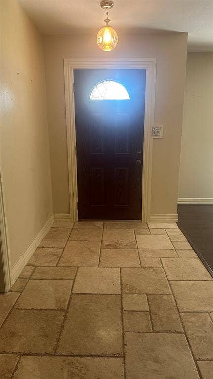 Entryway featuring varied-size floor tiles, a dark wood-finish door with a decorative glass insert, and an overhead pendant light fixture