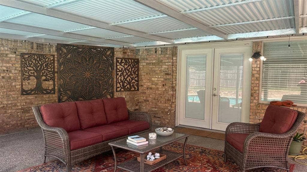Staged AI furniture;  Covered patio featuring a corrugated translucent ceiling, exposed brick wall, and French patio doors.