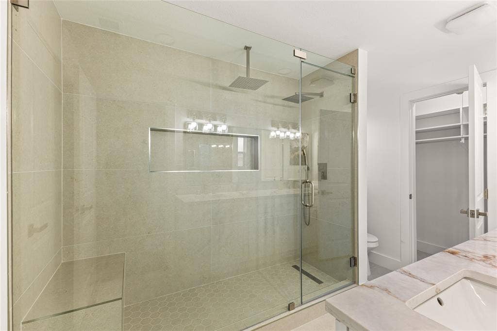 2716 Landershire Lane, Plano, TX 75023 Glass-enclosed shower with a built-in bench, dual rain shower heads, and recessed niche