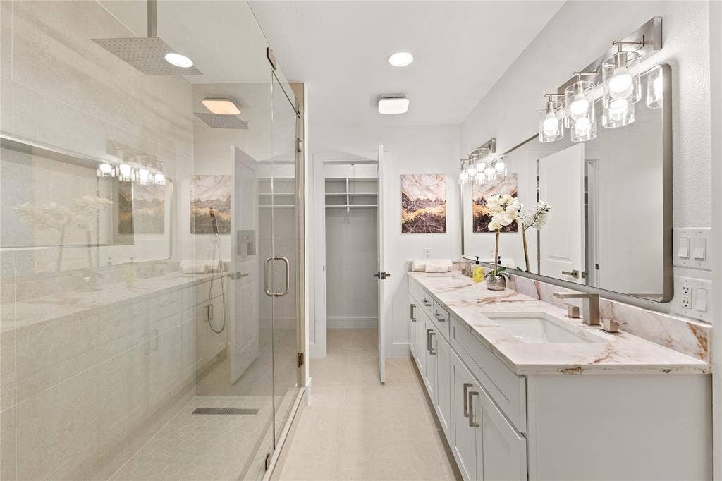 2716 Landershire Lane, Plano, TX 75023 Dual vanity with integrated sinks and stone countertops, glass-enclosed shower with rain showerhead, recessed lighting, and an open closet with built-in shelving