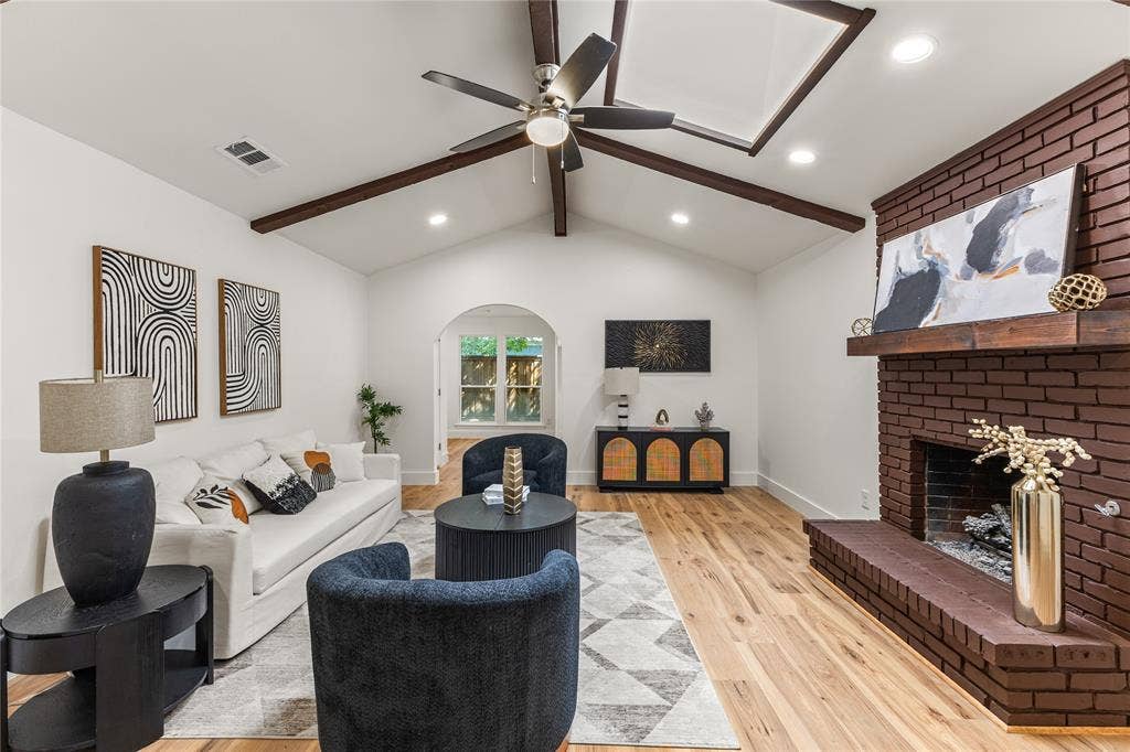 2716 Landershire Lane, Plano, TX 75023 Vaulted ceiling with exposed wood beams, a prominent brick fireplace, wood-finish flooring, and recessed lighting
