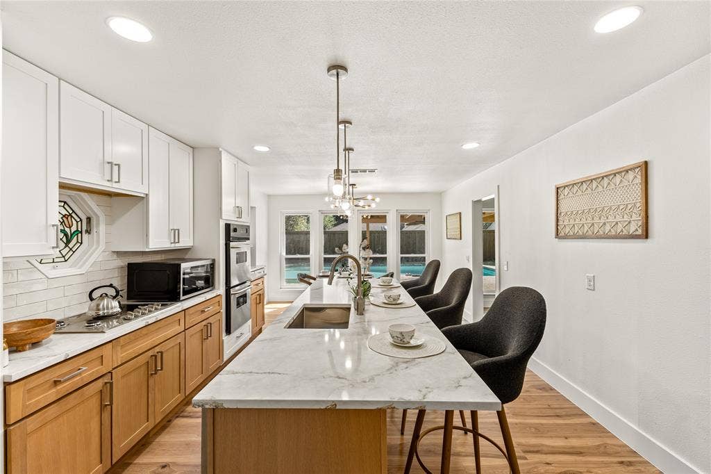 2716 Landershire Lane, Plano, TX 75023 Modern kitchen featuring a large island with seating, a stainless steel sink, dual-tone cabinetry, double wall ovens, and recessed lighting
