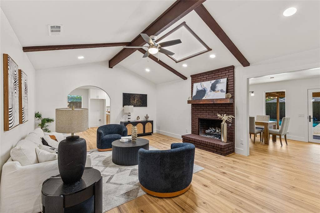2716 Landershire Lane, Plano, TX 75023 Vaulted ceiling with exposed wood beams, brick-clad fireplace with mantel, recessed lighting, wood-finish flooring, and an arched doorway