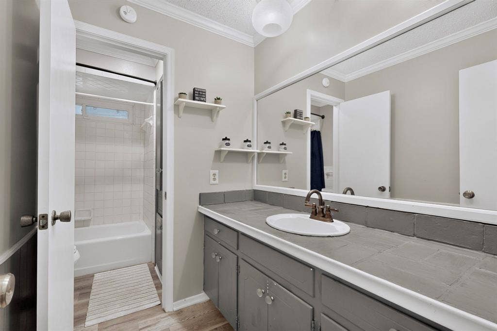1418 Stony Brook Lane, Garland, TX 75043 Vanity with an integrated sink and bronze-finish faucet, a full-width wall mirror, and wood-finish flooring
