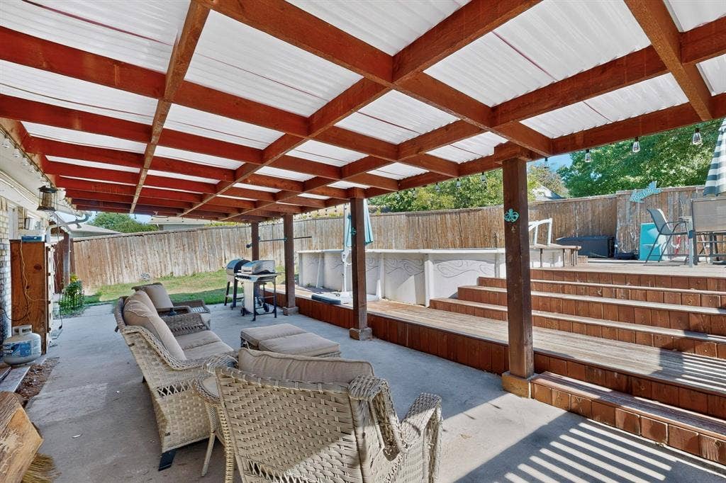 1418 Stony Brook Lane, Garland, TX 75043 Covered concrete patio with an adjacent multi-level wood deck, supported by substantial wood columns and featuring a privacy fence