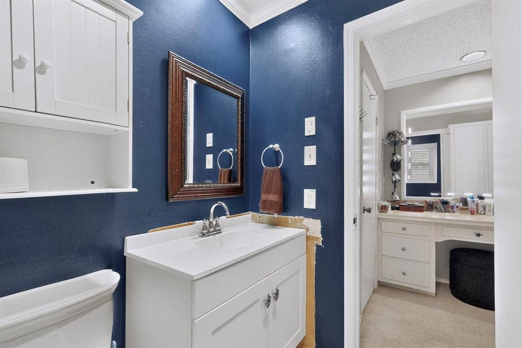 1418 Stony Brook Lane, Garland, TX 75043 White vanity with a single basin sink, wall-mounted mirror, and white overhead cabinetry