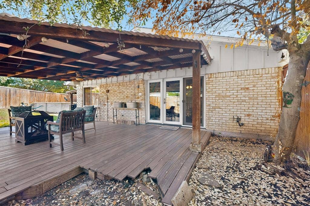 1418 Stony Brook Lane, Garland, TX 75043 Expansive wood-finish deck with a substantial overhead pergola, dual sets of French doors, and a brick exterior