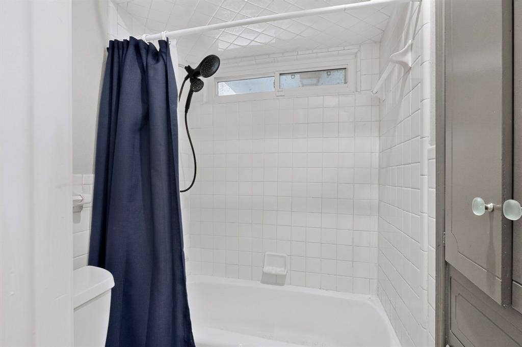 1418 Stony Brook Lane, Garland, TX 75043 White subway tile shower surround with a built-in bathtub, a window, and an adjacent built-in cabinet