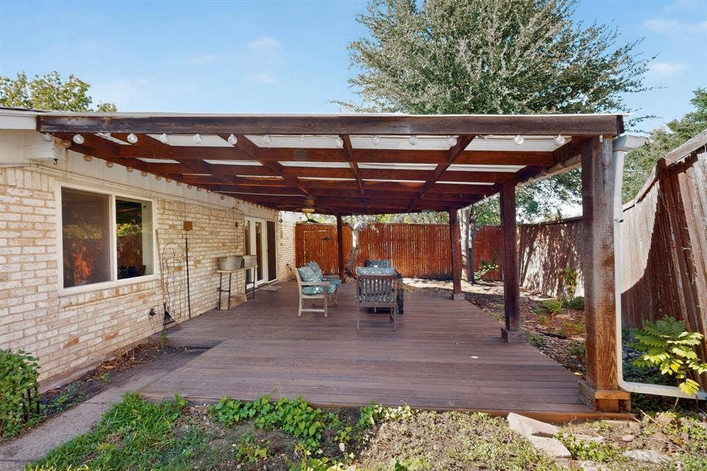 1418 Stony Brook Lane, Garland, TX 75043 Expansive wood-finish deck with a substantial wooden pergola, supported by robust columns, featuring string lighting