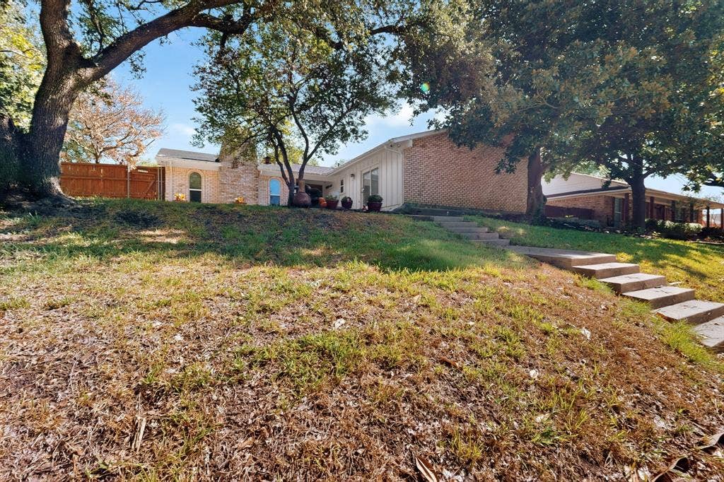 1418 Stony Brook Lane, Garland, TX 75043 Brick exterior residence with a sloped front yard, concrete steps, and mature trees