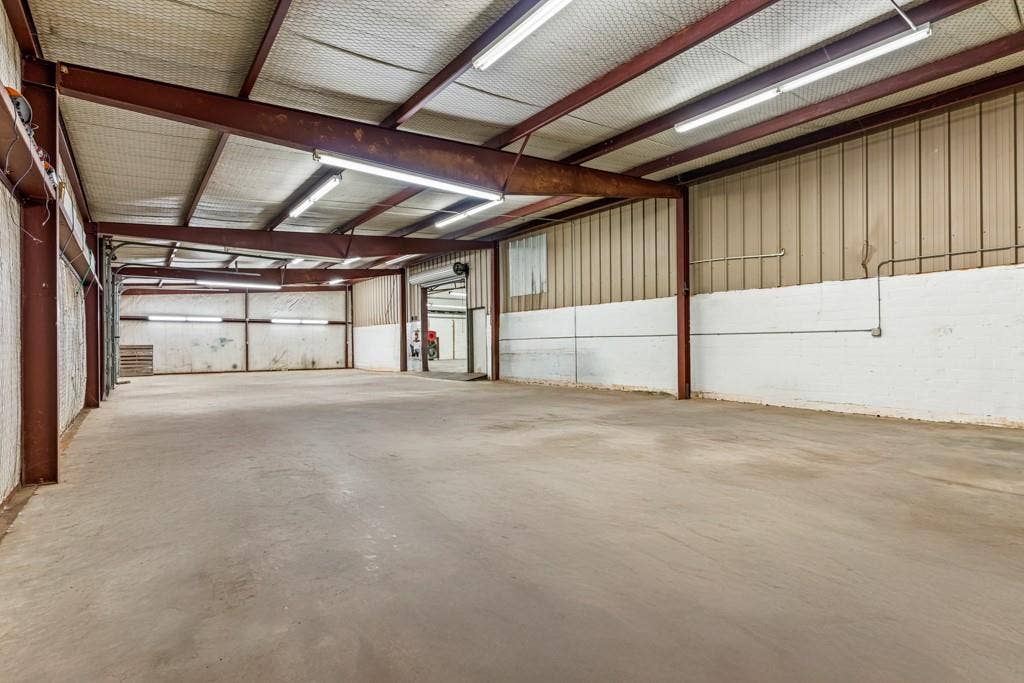 414 E Marshall Street, Gilmer, TX 75644 Spacious interior featuring exposed structural beams, a concrete floor, corrugated metal walls, and fluorescent lighting fixtures