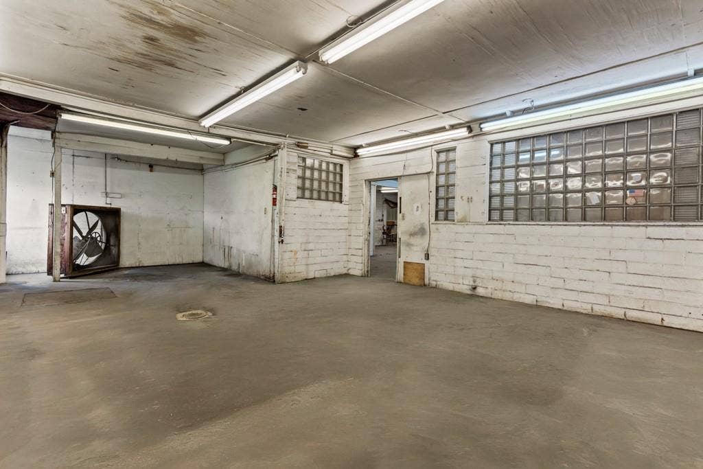 414 E Marshall Street, Gilmer, TX 75644 Concrete flooring, exposed ceiling with fluorescent lighting, painted brick walls, glass block windows, and an industrial-style wall fan