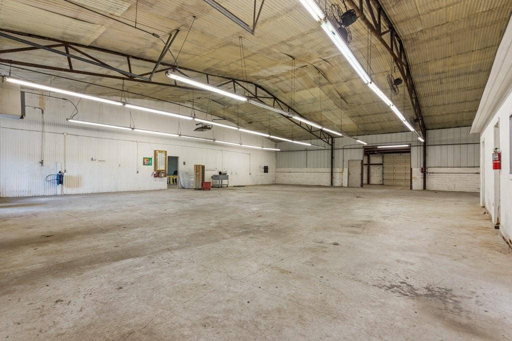 414 E Marshall Street, Gilmer, TX 75644 Expansive open warehouse space featuring concrete flooring, corrugated metal walls, exposed structural beams, and fluorescent overhead lighting