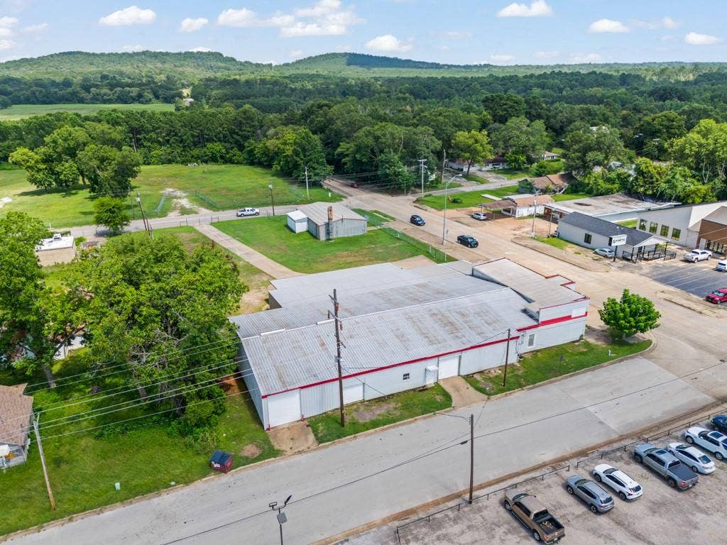 414 E Marshall Street, Gilmer, TX 75644 Commercial property with a metal roof, white siding, and red trim, featuring a paved parking area and an adjacent green space