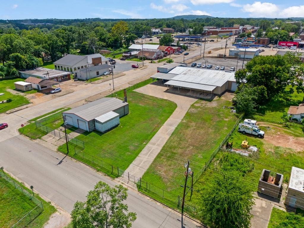 414 E Marshall Street, Gilmer, TX 75644 Two commercial buildings with metal roofing, expansive paved driveways, a large open lot, and perimeter fencing