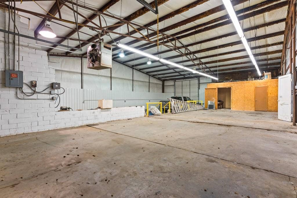 414 E Marshall Street, Gilmer, TX 75644 Concrete flooring, exposed metal ceiling trusses, fluorescent strip lighting, white brick wall, built-in storage area
