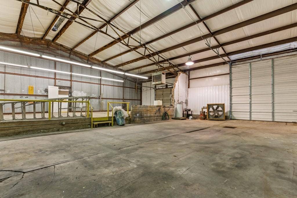 414 E Marshall Street, Gilmer, TX 75644 Expansive concrete floor, industrial lighting fixtures, metal roll-up door, loading dock with yellow handrails, and exposed steel truss ceiling