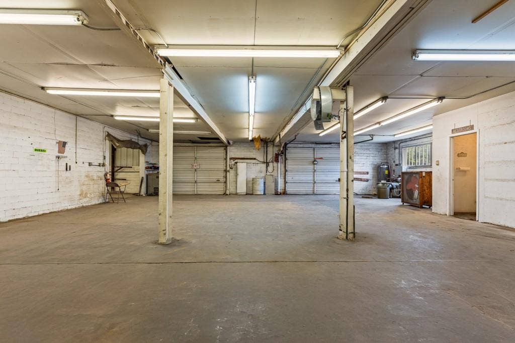 414 E Marshall Street, Gilmer, TX 75644 Spacious interior featuring concrete flooring, white brick walls, multiple overhead fluorescent light fixtures, and two overhead garage doors