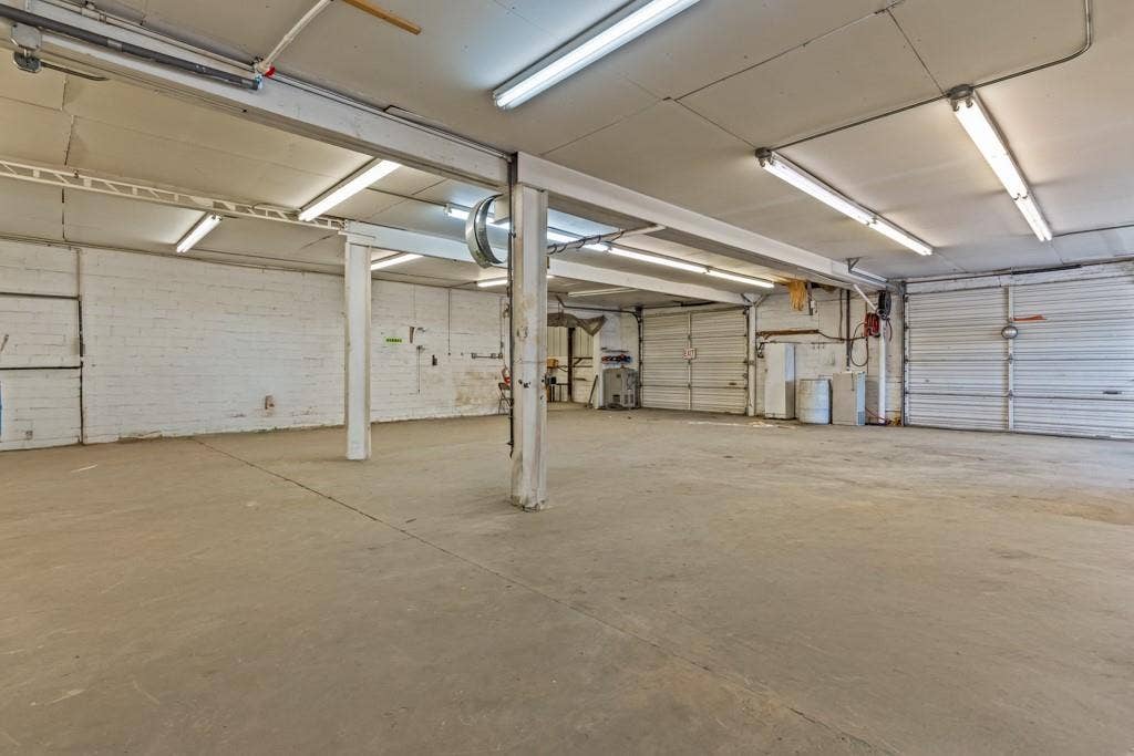 414 E Marshall Street, Gilmer, TX 75644 Spacious interior with concrete flooring, multiple overhead fluorescent light fixtures, and several roll-up garage doors