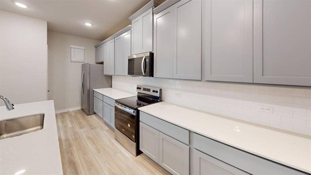 Kitchen featuring light wood-finish flooring, light gray cabinetry, white countertops, and a subway tile backsplash