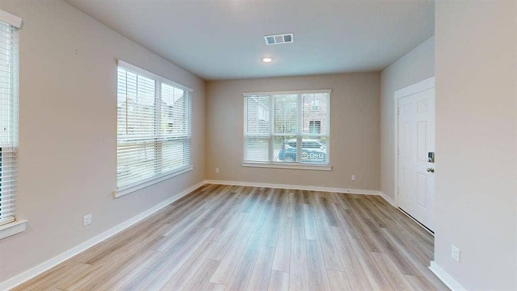 Light wood-finish flooring, recessed lighting, multiple windows with blinds, and a white paneled entry door