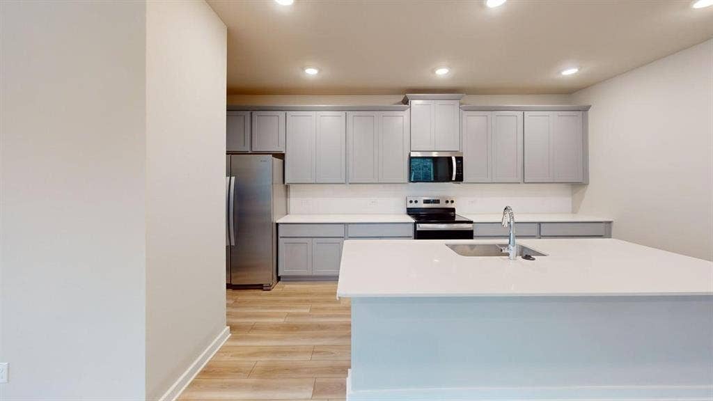 Kitchen featuring light gray cabinetry, white countertops, stainless steel appliances, and wood-finish flooring