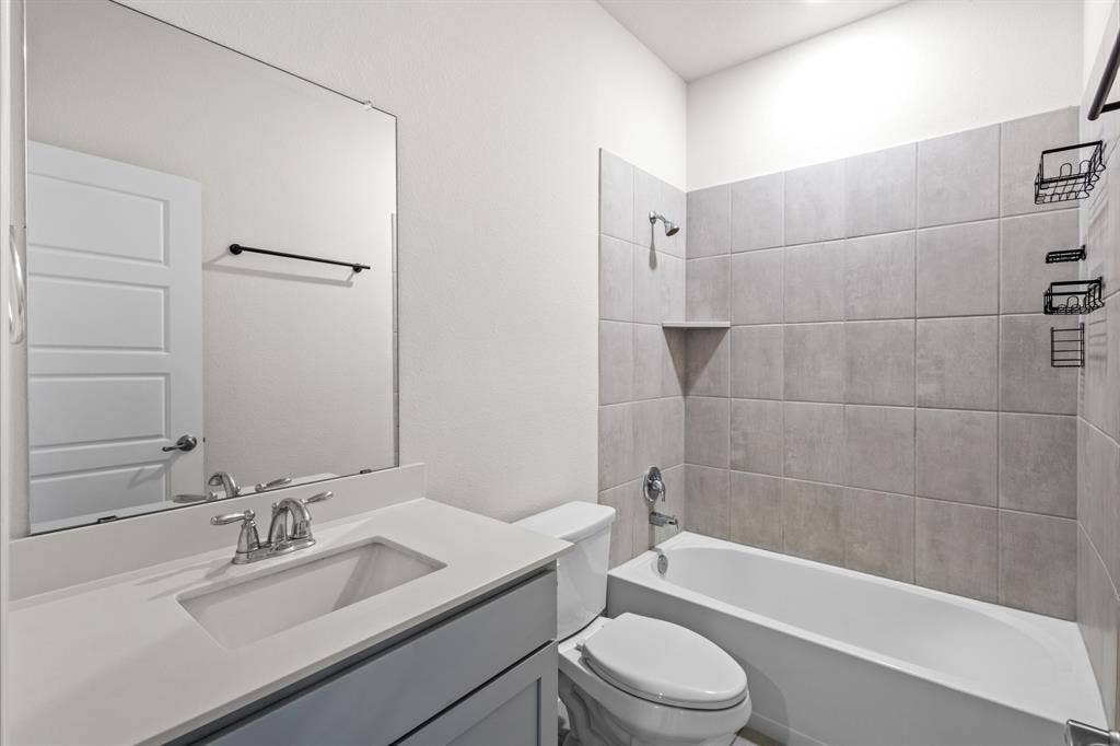 1536 Estivella Drive, Little Elm, TX 75068 Bathroom featuring a single vanity with an undermount sink, a large wall-mounted mirror, a toilet, and a combination shower and tub with tile surround