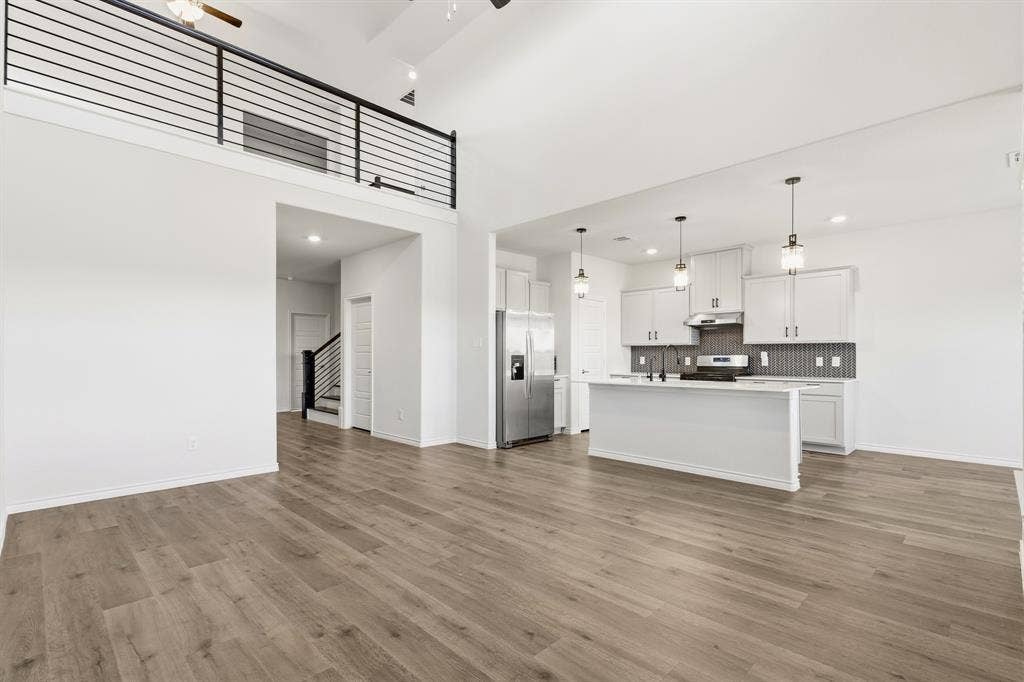 1536 Estivella Drive, Little Elm, TX 75068 Open-concept living and kitchen area featuring wood-finish flooring throughout, soaring ceilings with pendant lighting, and a modern kitchen with white cabinetry and dark tile backsplash