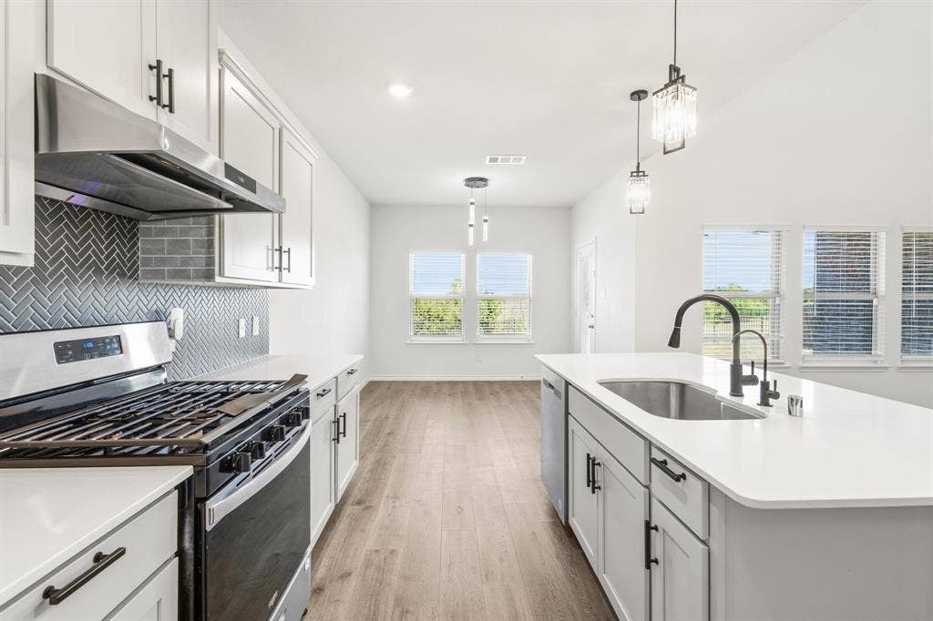 1536 Estivella Drive, Little Elm, TX 75068 Modern kitchen featuring white cabinetry, a herringbone tile backsplash, stainless steel appliances, and an island with an undermount sink