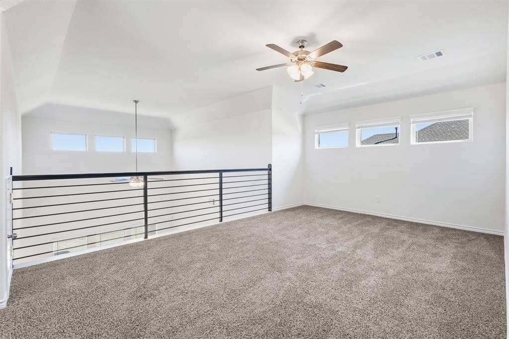 1536 Estivella Drive, Little Elm, TX 75068 Carpeted loft space featuring multiple windows, a ceiling fan, and a contemporary horizontal bar railing