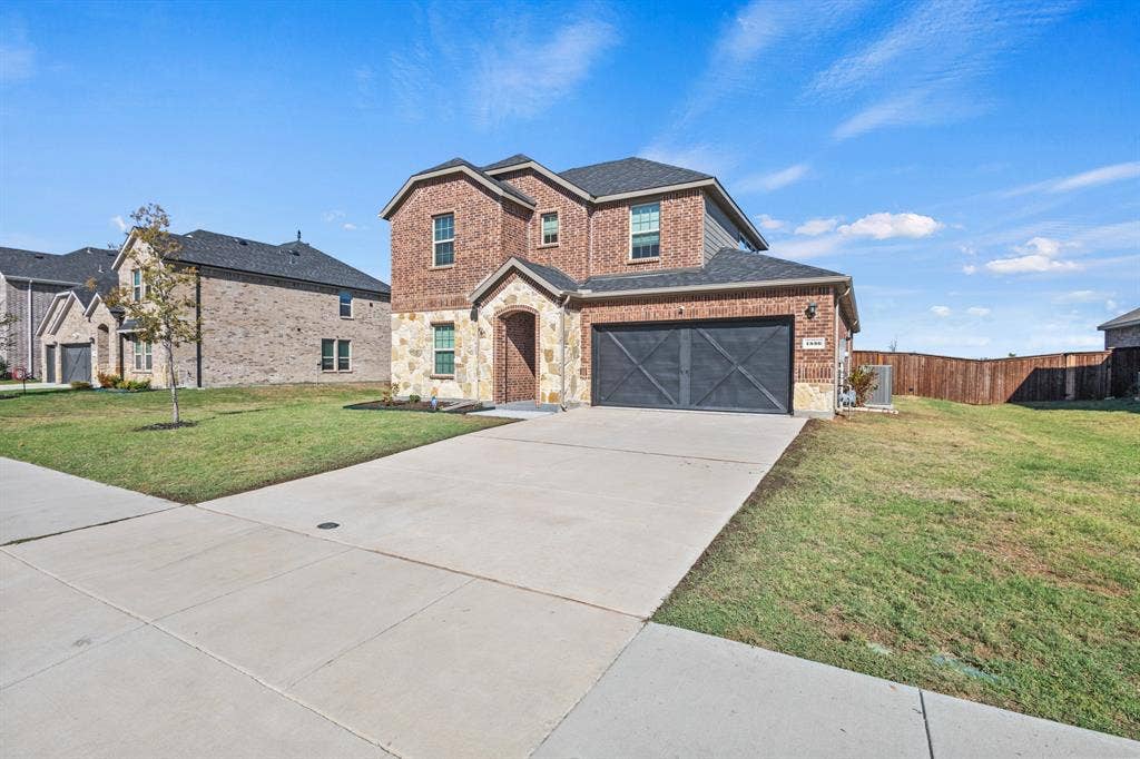 1536 Estivella Drive, Little Elm, TX 75068 Two-story brick and stone residence featuring a two-car garage with dark paneled doors, established landscaping with mature lawn, and a wide concrete driveway