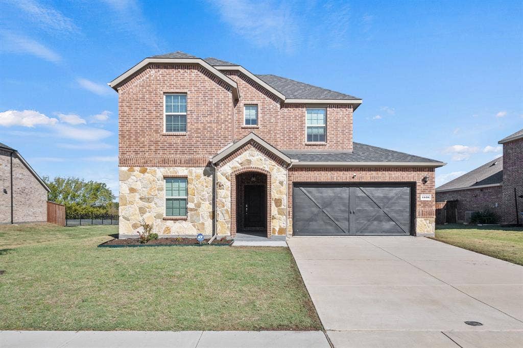 1536 Estivella Drive, Little Elm, TX 75068 Two-story brick and stone facade, arched entry, dark garage door with decorative trim, concrete driveway, and manicured front lawn