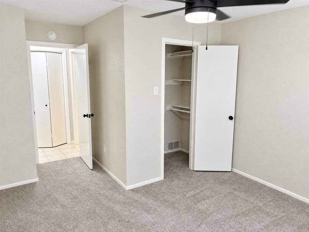 Neutral-toned carpeting, matte black hardware, built-in closet shelving, and a ceiling fan with integrated light fixture