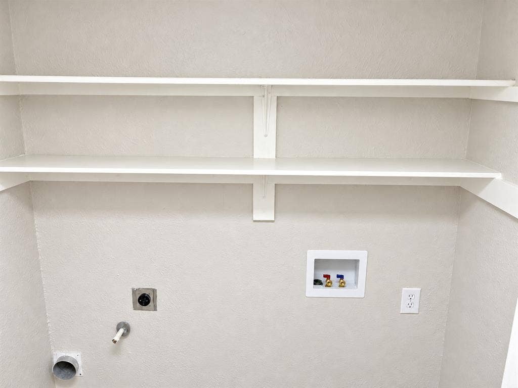 Utility area featuring two levels of built-in shelving, recessed water supply valves, and dedicated electrical and venting connections