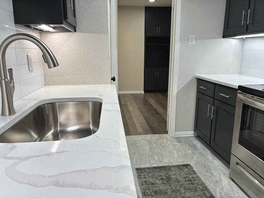 Kitchen featuring quartz countertops, undermount stainless steel sink with pull-down faucet, white subway tile backsplash, dark-toned cabinetry, and stainless steel appliance