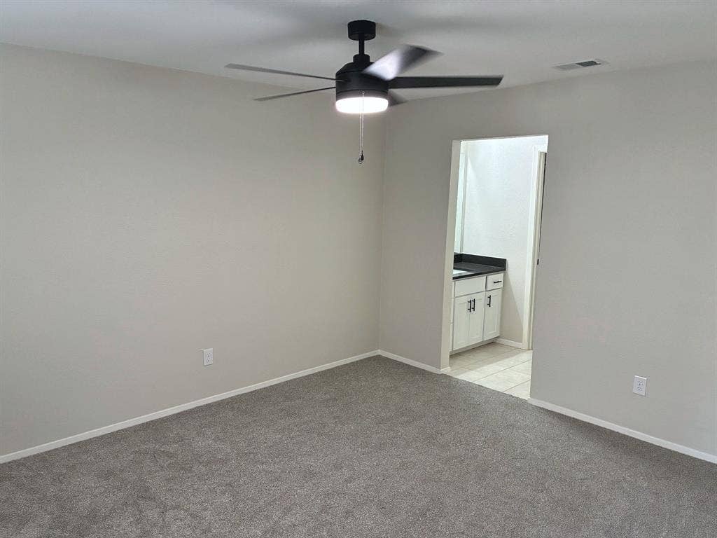 Neutral-toned carpeting, matte black ceiling fan with integrated LED lighting, and vanity featuring a solid surface countertop with dark hardware