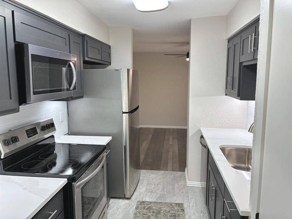 Kitchen featuring dark shaker-style cabinetry, stainless steel appliances, white solid-surface countertops, subway tile backsplash, and stone-finish flooring