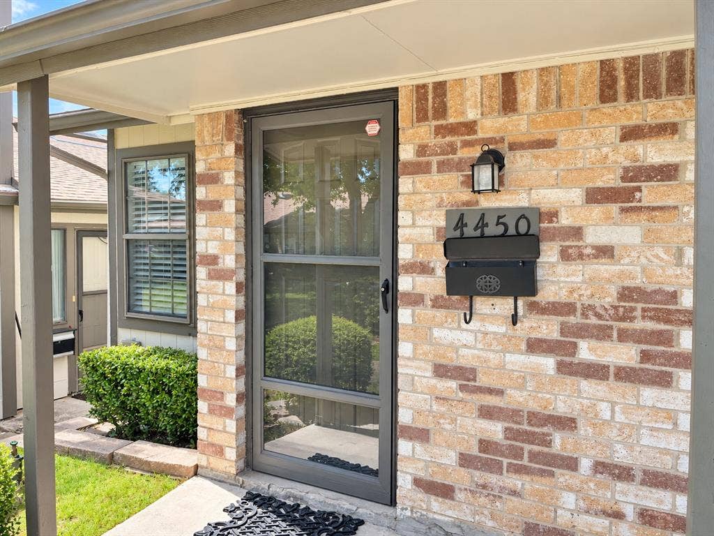 Exterior entryway featuring a multi-tone brick facade, full-length metal storm door, wall-mounted matte black mailbox with integrated address plaque, and dark metal exterior lighting fixture