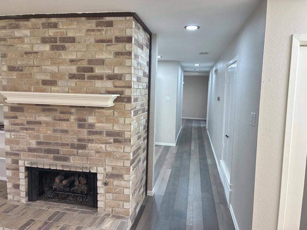 Floor-to-ceiling multi-tone brick fireplace featuring a wood mantel, integrated flush-mount recessed lighting, and multi-tone wood-finish flooring