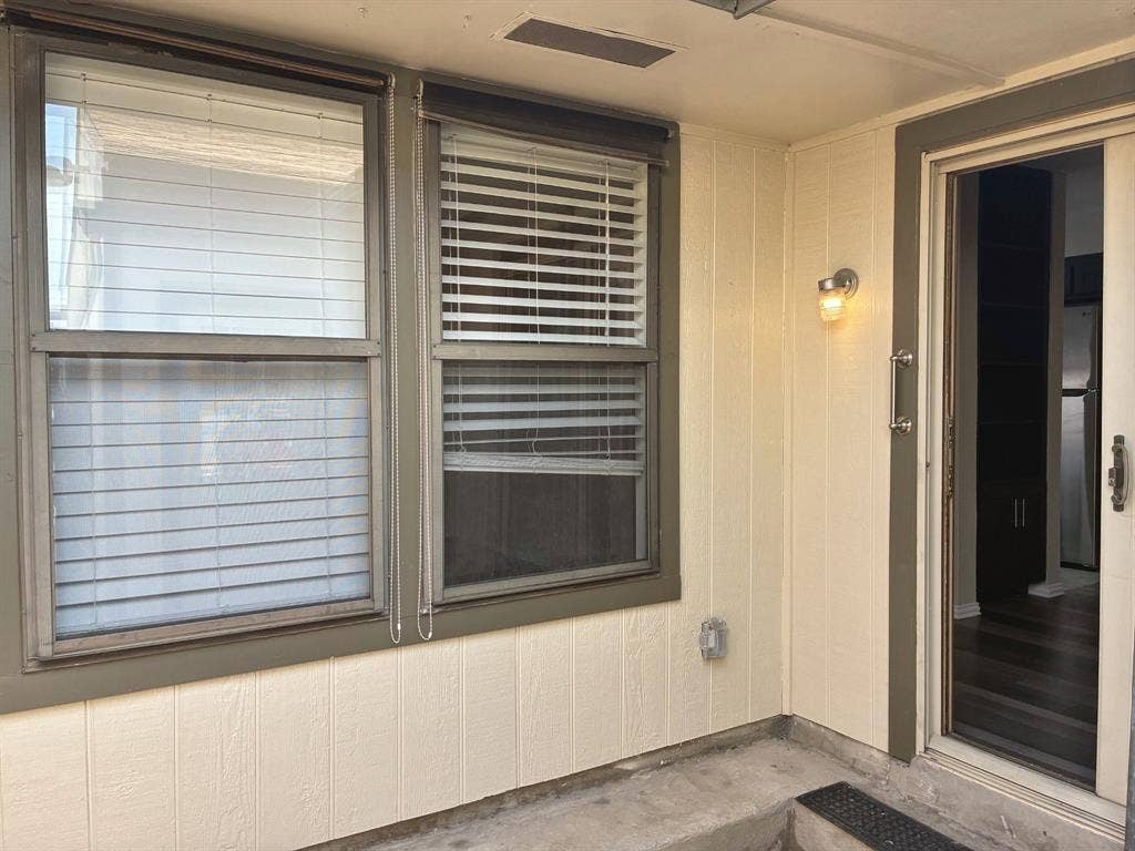 Exterior featuring vertical siding, dual-pane windows with integrated blinds, and a glass-panel storm door with metallic hardware