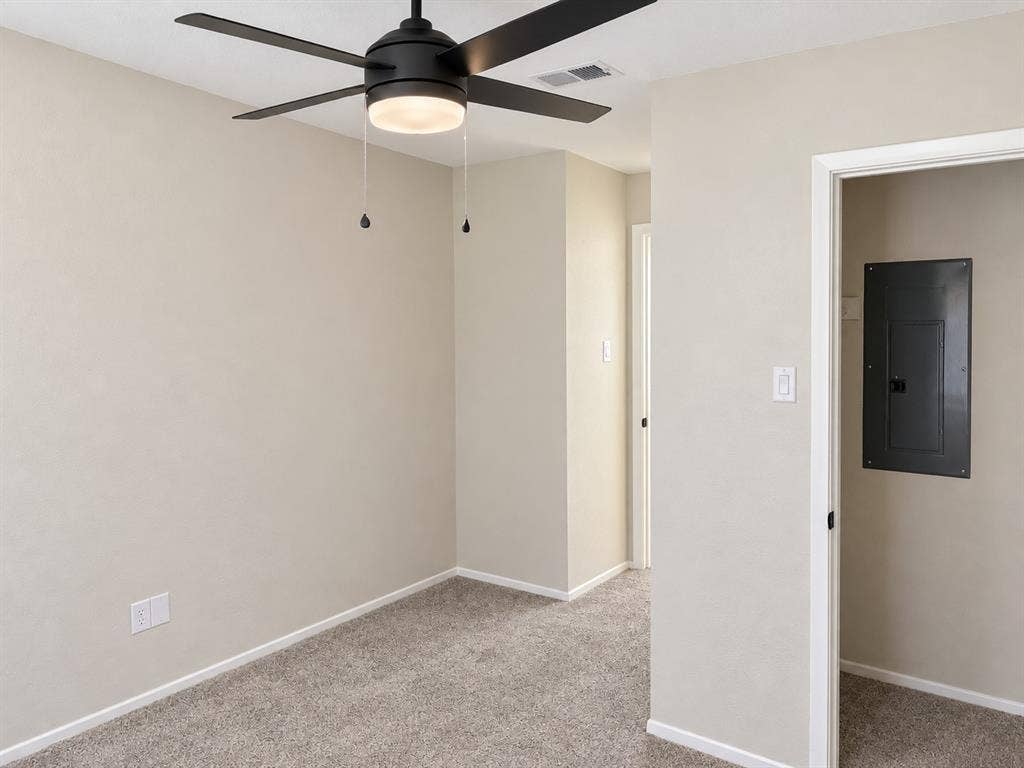Interior room featuring neutral wall paint, carpeted flooring, and a modern black ceiling fan with integrated lighting